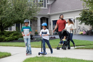 Some Kids on their Scooters with their parents walking behind them.